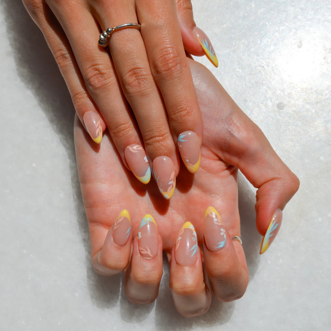 Set de faux ongles press-on faits main Secret Garden dans une boîte transparente, avec french jaune pastel et motifs floraux délicats.