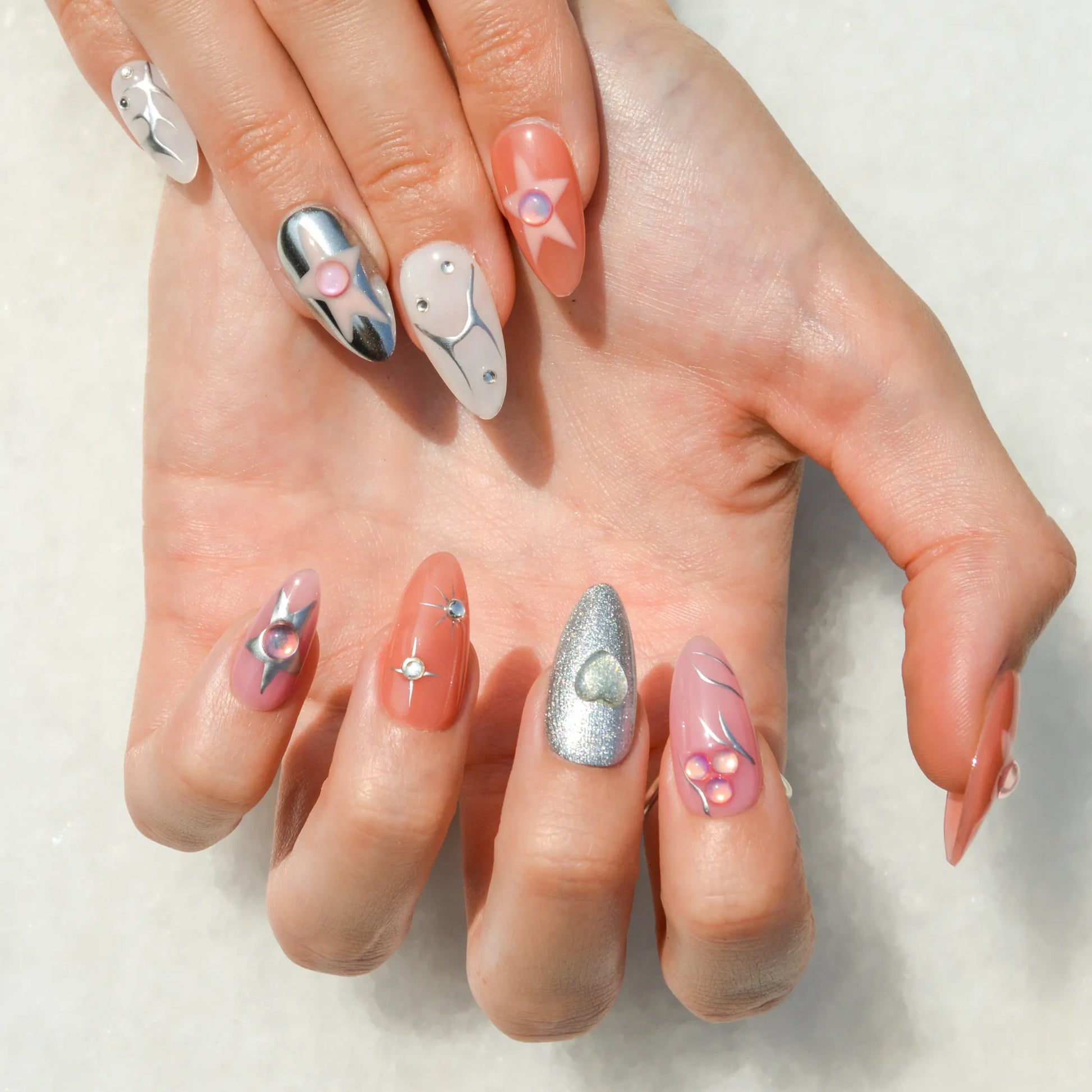 Faux ongles Metallic Muse en gel et acrylique, mélange de rose, blanc, chrome et motifs 3D.