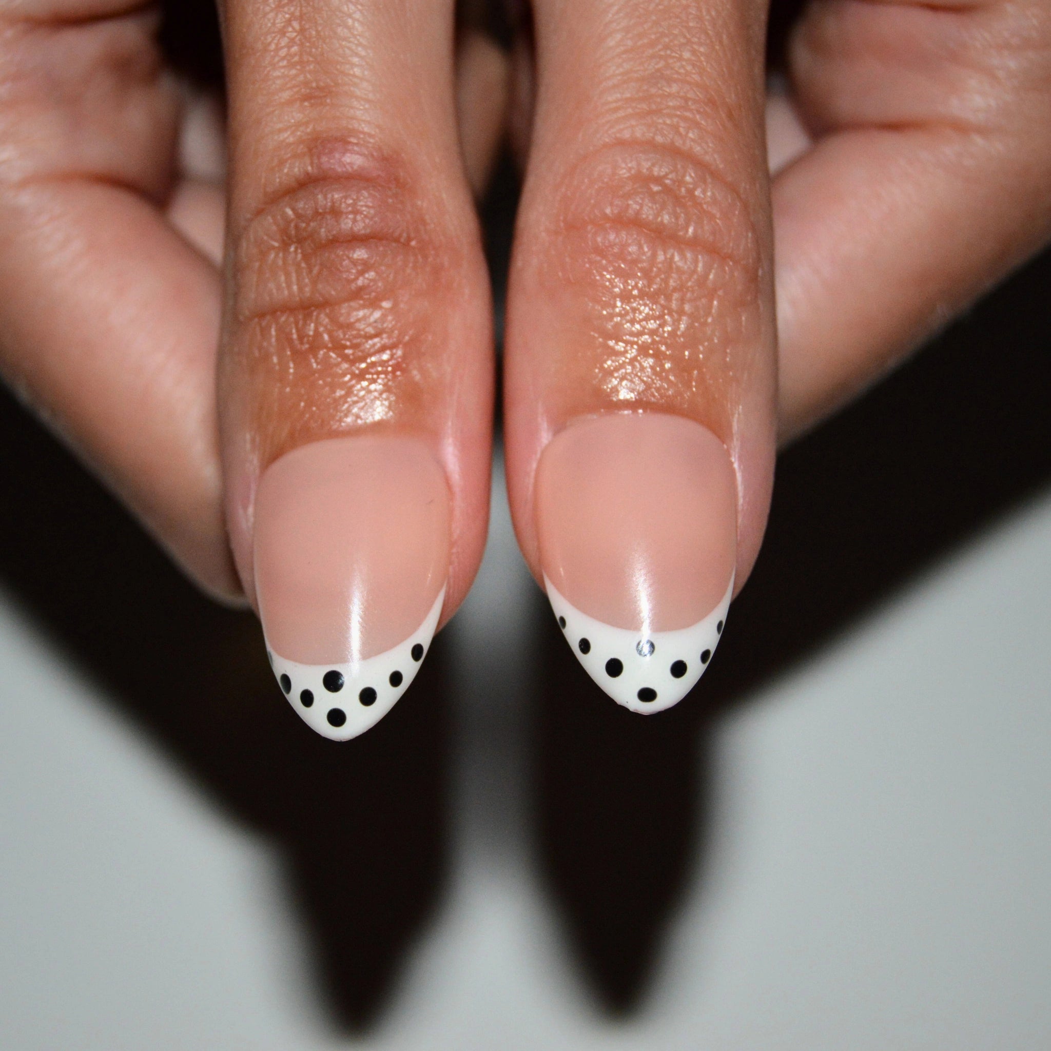 Gros plan sur des press-on nails nude à french blanche ornée de pois noirs, réalisés à la main en gel et acrylique – modèle Polka Dots