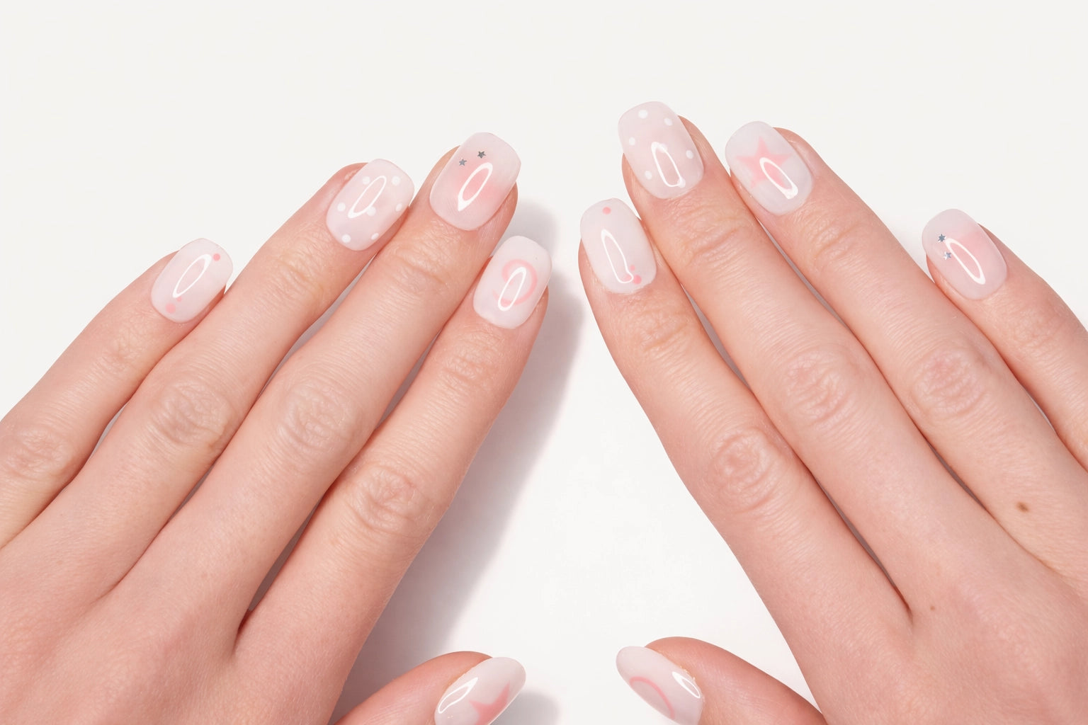 Faux ongles press-on Pink Dream portés sur la main — étoiles roses et pois blancs sur base blanche et rose pâle — Mimi Press-On