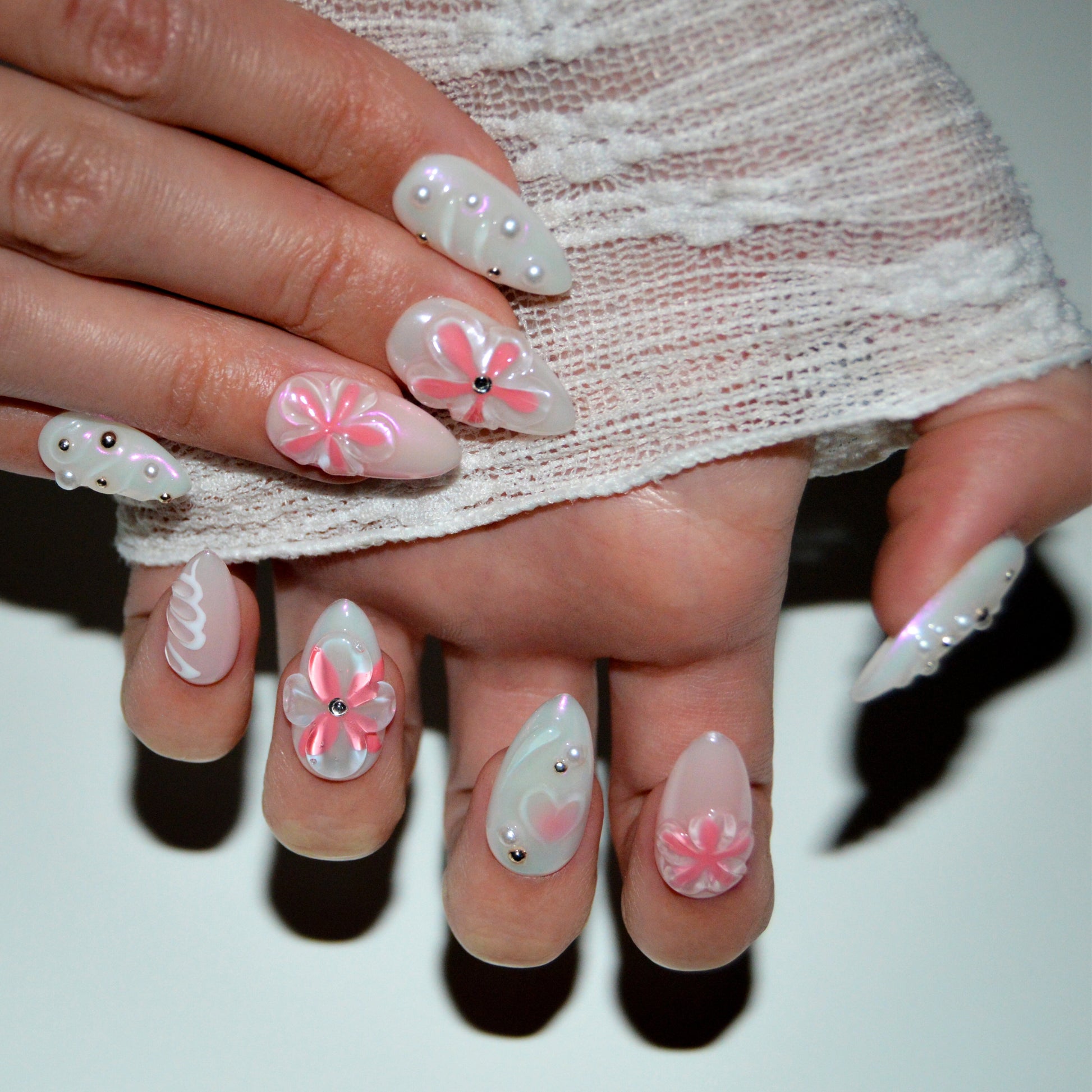 Press-on nails Pink Fever posés sur les mains, fleurs 3D roses et détails nacrés, finition artisanale en gel et acrylique.