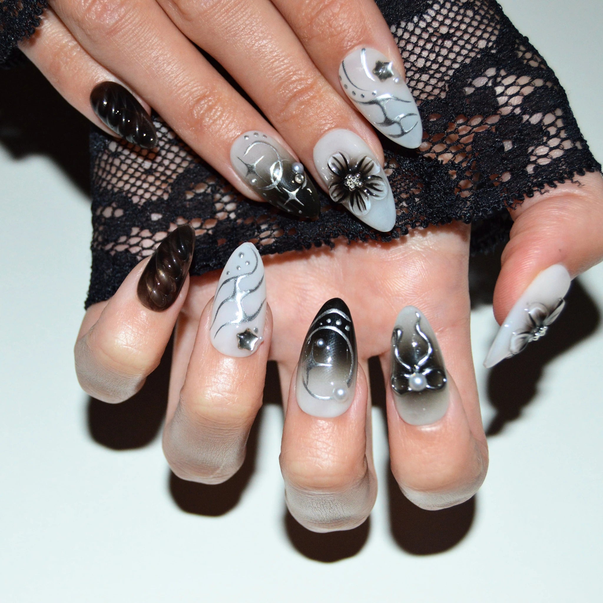 Vue rapprochée des press-on nails Shadow Petal portés, mélange de designs 3D noir et blanc avec fleurs, nœuds et dégradés en gel et acrylique.