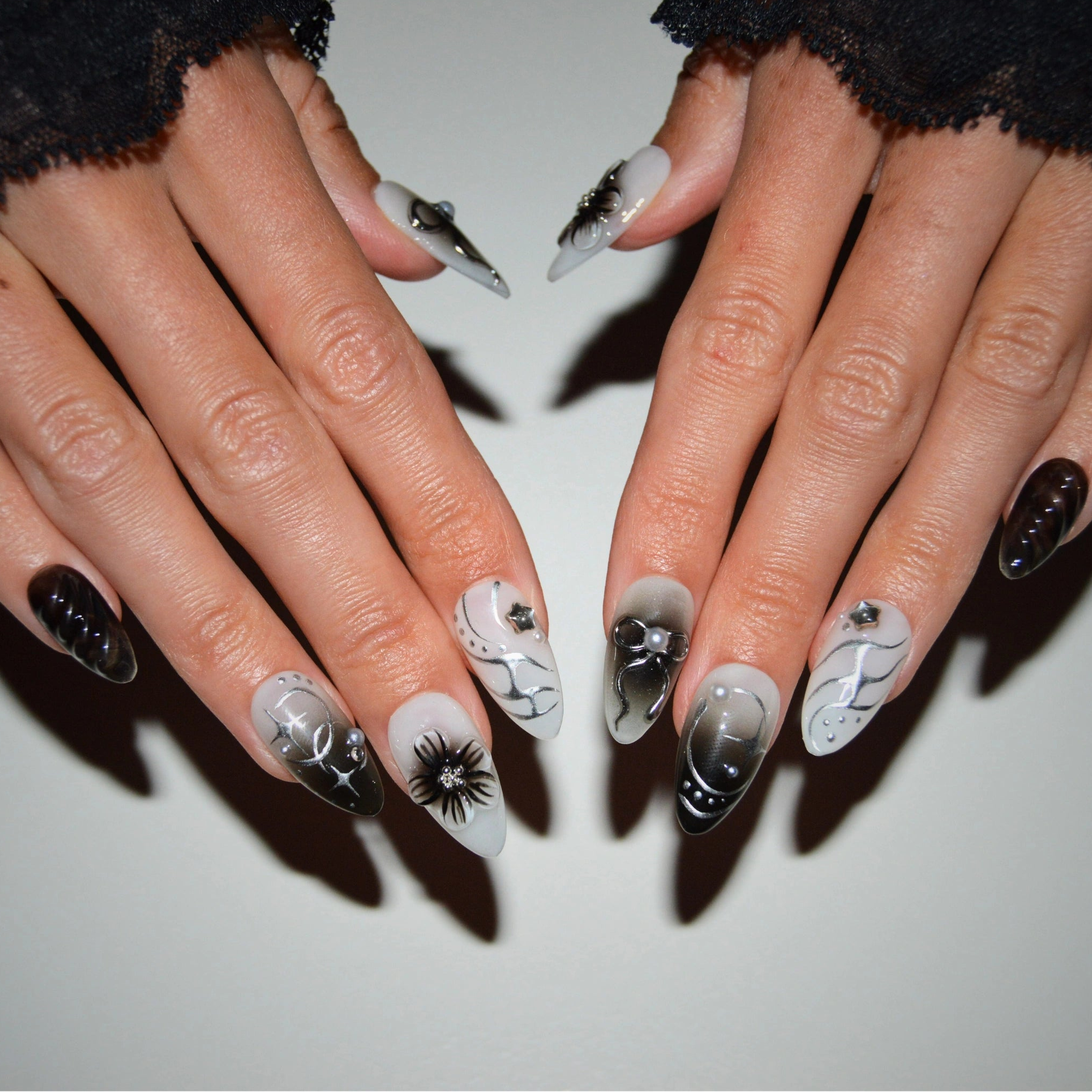 Vue complète des press-on nails Shadow Petal portés, mélange de designs 3D noir et blanc avec fleurs, nœuds et dégradés en gel et acrylique.