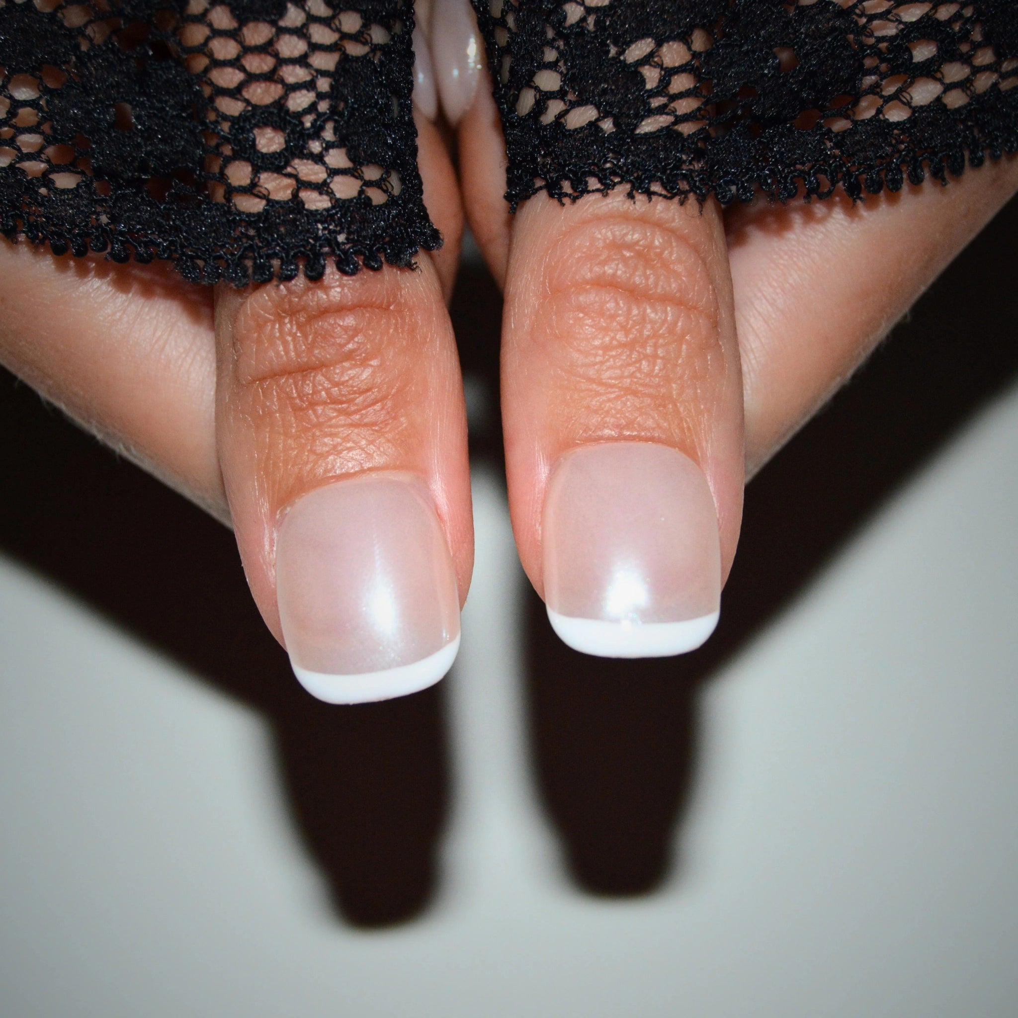 Ongles press-on carrés French blancs, faits main en gel et acrylique haut de gamme, portés sur deux doigts.