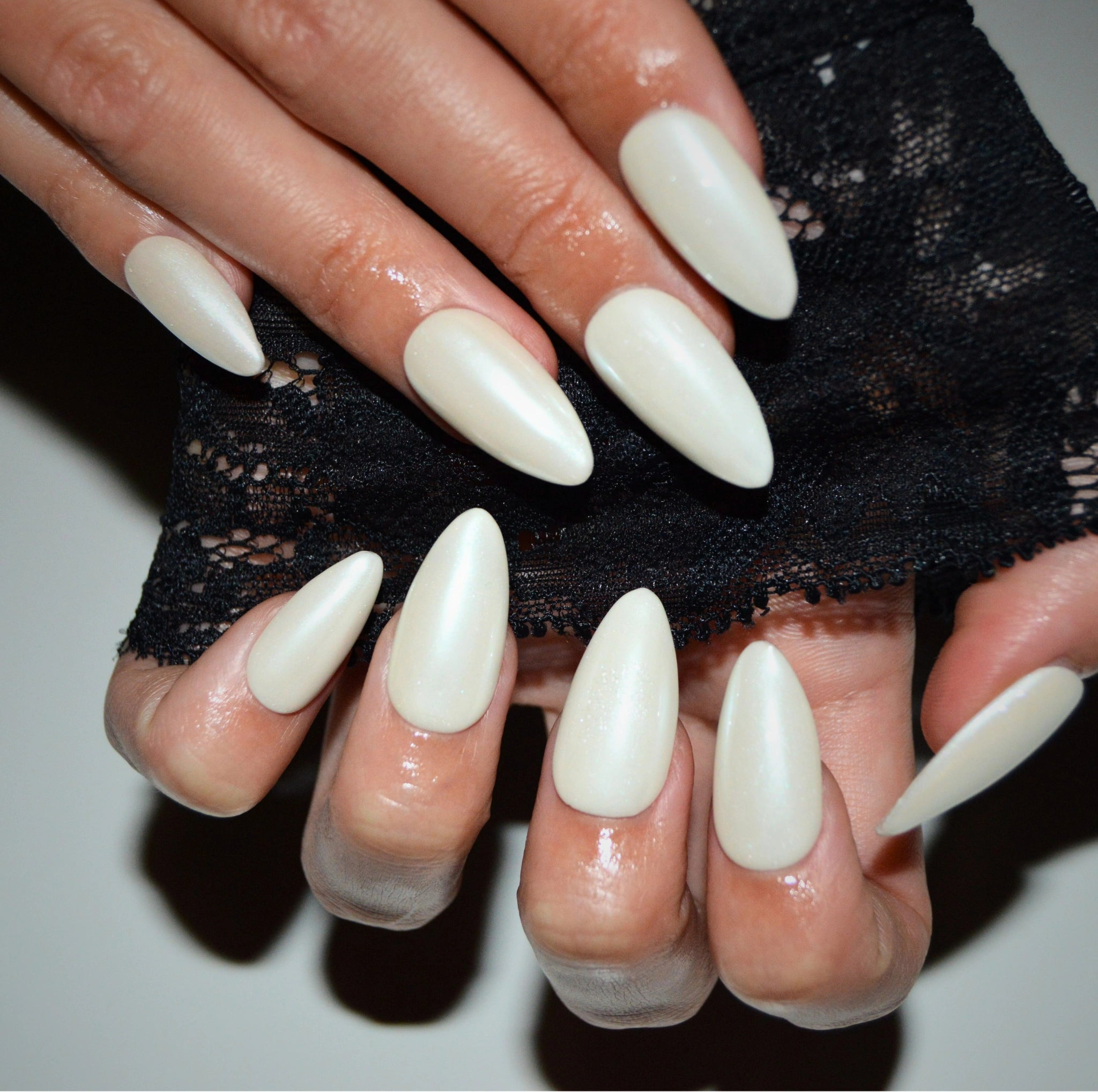 Press-on nails Winter Glaze portés, finition blanche nacrée brillante, vue rapprochée avec dentelle noire en arrière-plan.